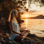 Woman meditating by the lake at sunset.