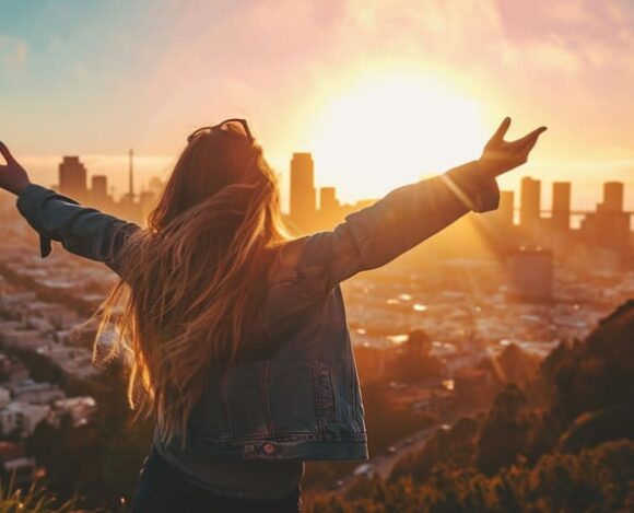 Woman celebrating with arms raised overlooking city skyline at sunrise