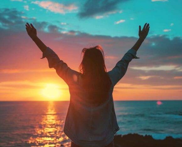Woman raising arms in celebration at sunset by the sea