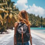Woman with backpack walking on tropical beach with palm trees and clear blue water