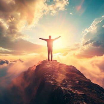 Person standing on mountain top with arms raised above clouds at sunrise