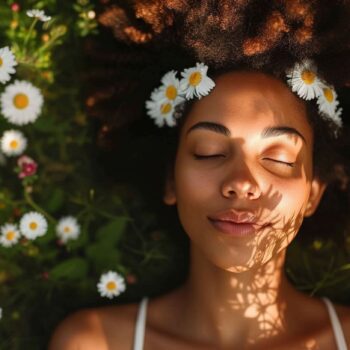 Young woman relaxing in a field of daisies with sunlight casting shadows on her face.