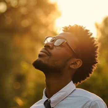 Man in white shirt and glasses looking up thoughtfully during golden hour.