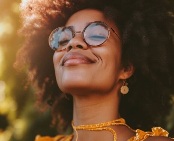 Happy African American woman with curly hair wearing glasses and smiling in sunlight
