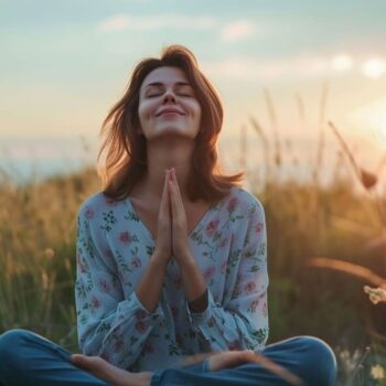Woman practicing meditation in lotus position at sunset in grassy field
