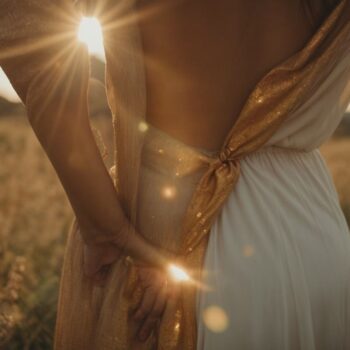 Woman in white dress with golden shawl standing in a field at sunset